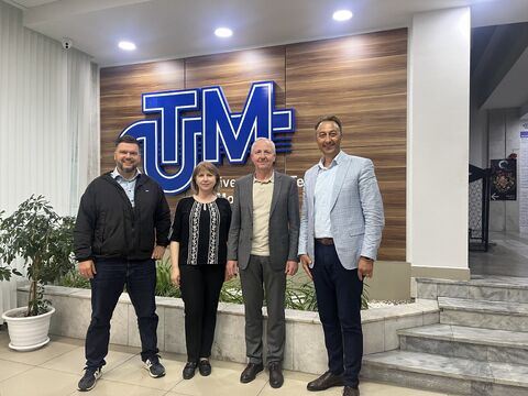 Eine Gruppe von vier Personen steht lächelnd nebeneinander in der Lobby der Technischen Universität von Moldau (UTM) in Chișinău. Ganz links befindet sich Stephan Hoffmann, der CEO von NorthIT. Im Hintergrund prallt das große, blau beleuchtete „UTM“-Logo an einer stilvollen Holzwand. Die Beteiligten posieren nach einem geschäftlichen und akademischen Austausch in einer hellen, modern gestalteten Universitätsumgebung.