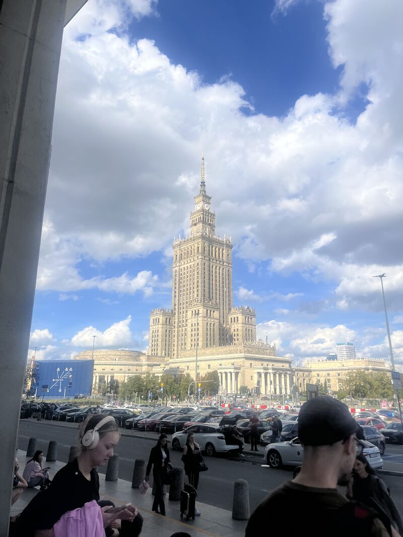 Eine Außenansicht des monumentalen Kultur- und Wissenschaftspalasts in Warschau unter einem leicht bewölkten, blauen Himmel.